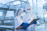Two staff members in protective clothing inspecting food production
