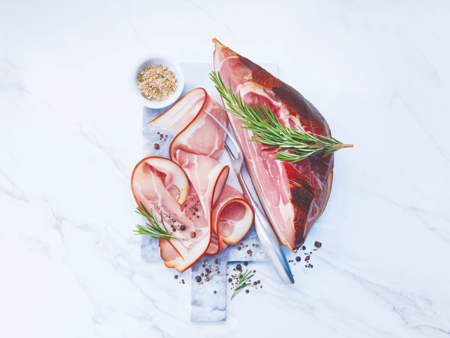 Raw ham slices with rosemary on marble