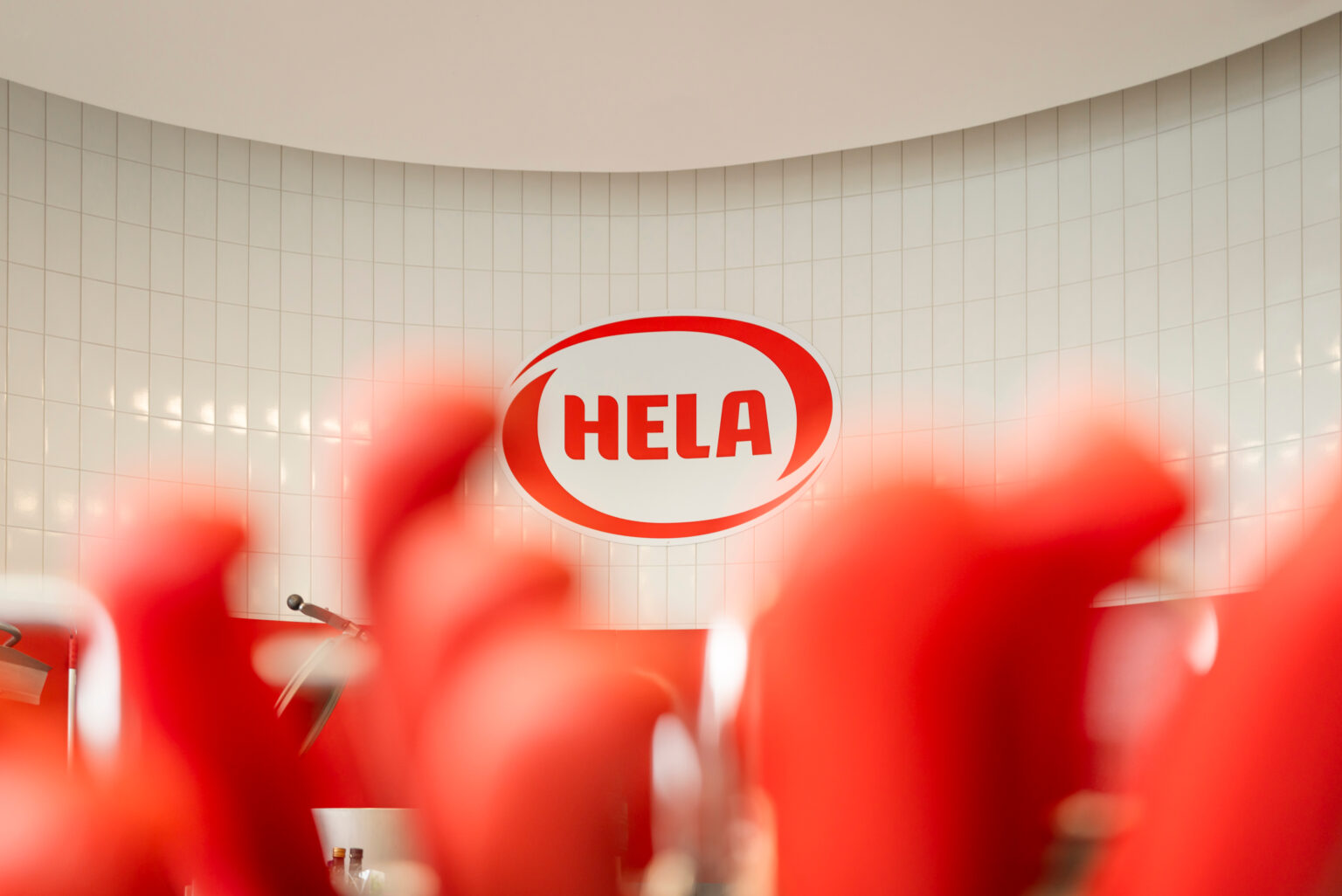 HELA logo on a wall behind red out-of-focus shapes