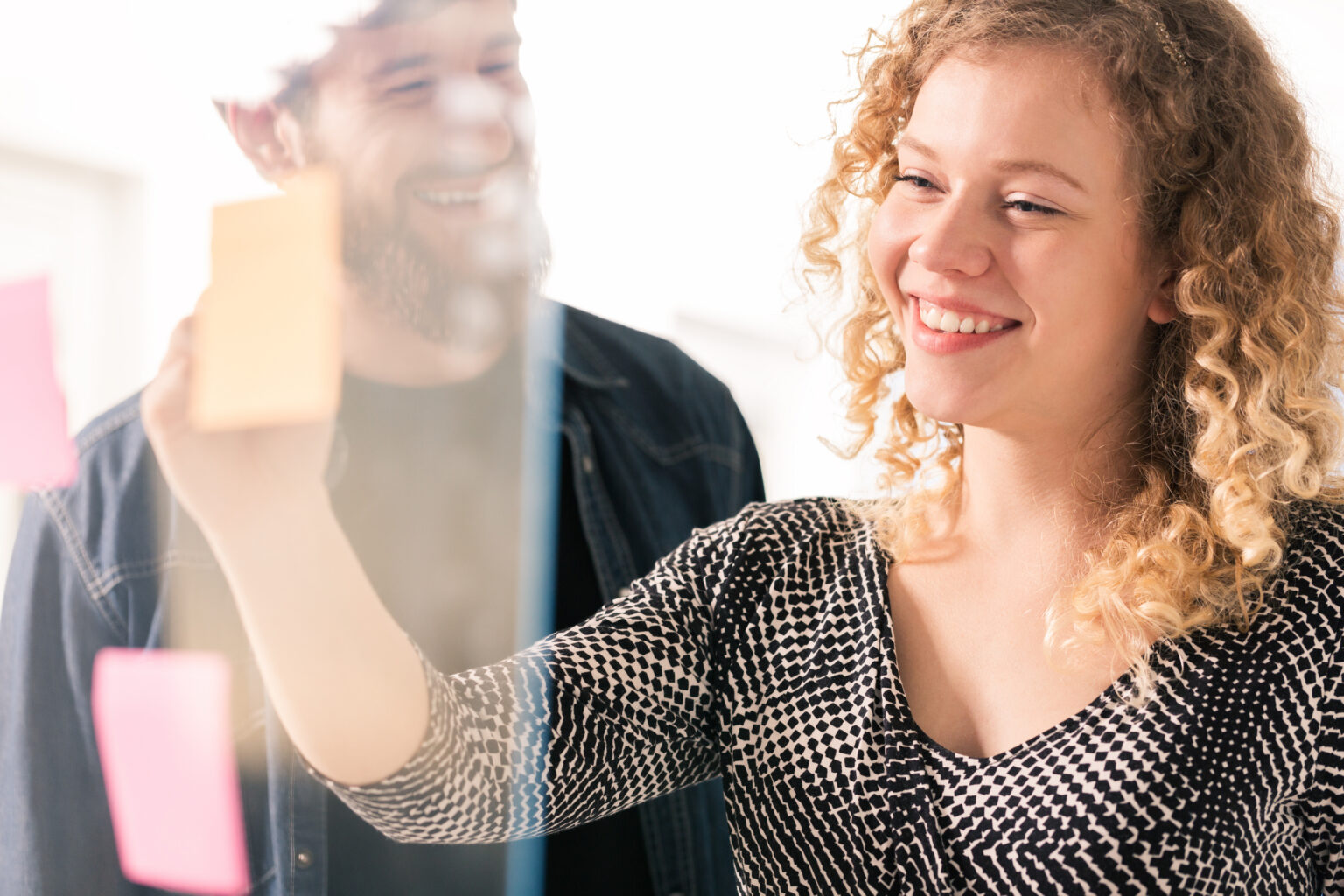 Smiling colleagues working with sticky notes on a glass wall