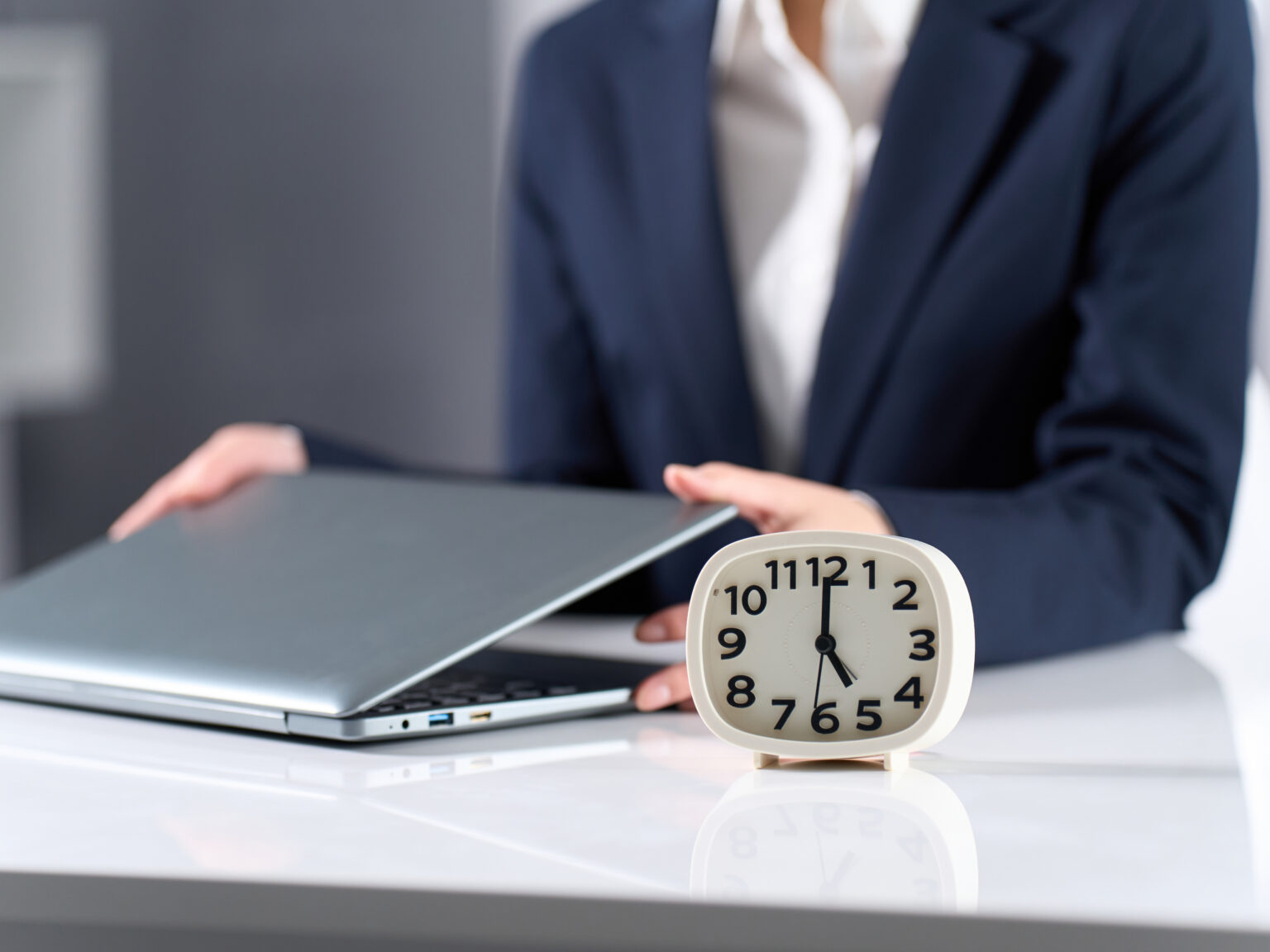 A person closing a laptop next to an alarm clock