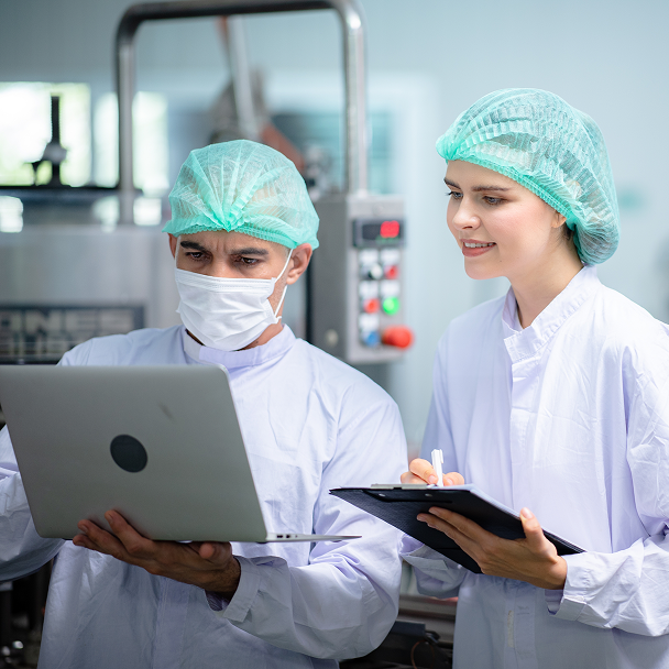 Two staff members in protective clothing reviewing data on a laptop