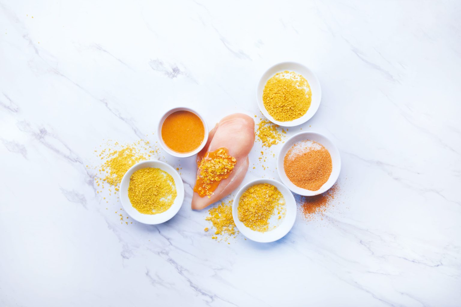 Chicken with bowls of coating ingredients